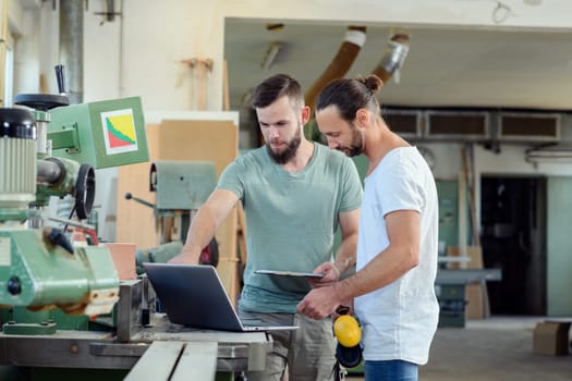 two worker in a carpenter's workshop with clipboard and computer