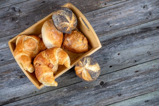 different fresh rolls and croissants in wooden basket in top view