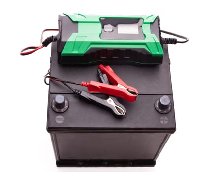 Black car accumulator battery and green charger isolated on a white background. Top view. Acid battery,12 volts supply. Concept of service, maintenance, charging car battery, diy
