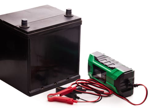 Black car accumulator battery and green charger isolated on a white background. Acid battery,12 volts supply. Concept of service, maintenance, charging car battery, diy
