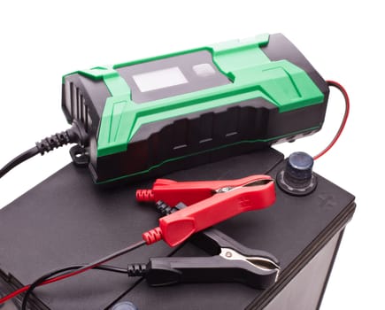 Black car accumulator battery and green charger isolated on a white background. Top view. Acid battery,12 volts supply. Concept of service, maintenance, charging car battery, diy