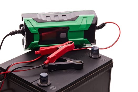 Black car accumulator battery and green charger isolated on a white background. Acid battery,12 volts supply. Concept of service, maintenance, charging car battery, diy