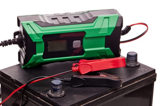 Black car accumulator battery and green charger isolated on a white background. Acid battery,12 volts supply. Concept of service, maintenance, charging car battery, diy