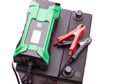 Black car accumulator battery and green charger isolated on a white background. Top view. Acid battery,12 volts supply. Concept of service, maintenance, charging car battery, diy