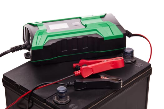 Black car accumulator battery and green charger isolated on a white background. Acid battery,12 volts supply. Concept of service, maintenance, charging car battery, diy