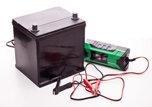 Black car accumulator battery and green charger isolated on a white background. Acid battery,12 volts supply. Concept of service, maintenance, charging car battery, diy