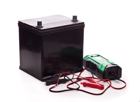 Black car accumulator battery and green charger isolated on a white background. Acid battery,12 volts supply. Concept of service, maintenance, charging car battery, diy