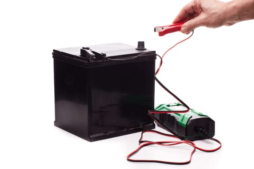 Black car accumulator battery and green charger isolated on a white background. Acid battery,12 volts supply. Concept of service, maintenance, charging car battery, diy