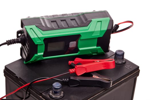 Black car accumulator battery and green charger isolated on a white background. Acid battery,12 volts supply. Concept of service, maintenance, charging car battery, diy