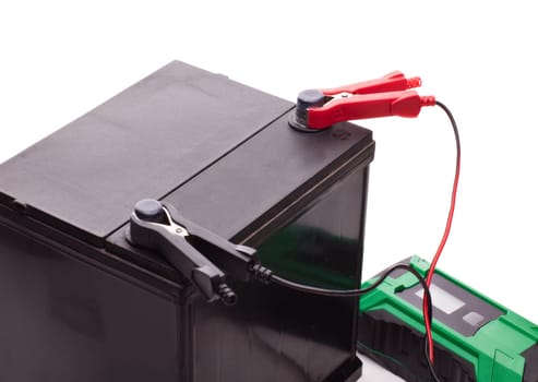 Black car accumulator battery and green charger isolated on a white background. Acid battery,12 volts supply. Concept of service, maintenance, charging car battery, diy