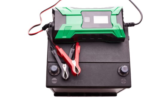 Black car accumulator battery and green charger isolated on a white background. Top view. Acid battery,12 volts supply. Concept of service, maintenance, charging car battery, diy