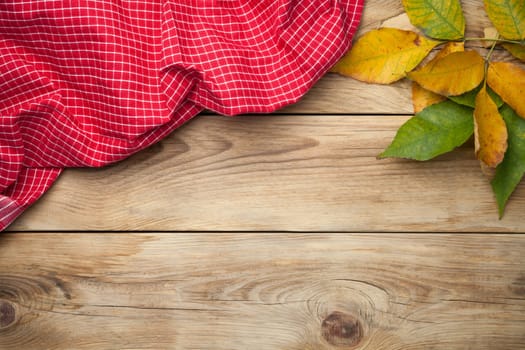 Red tablecloth and autumn leaves on wooden background. Top view. Copy space