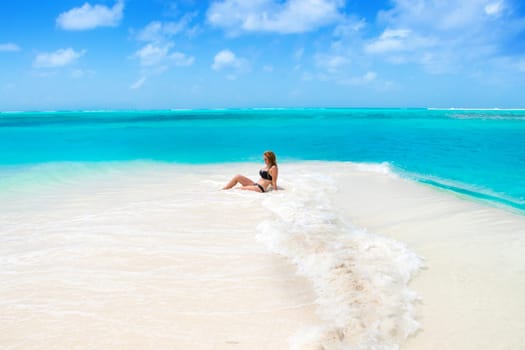 Blonde Girl in black bikini on dream beach at the turquoise ocean