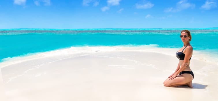 Blonde Girl in black bikini on dream beach at the turquoise ocean
