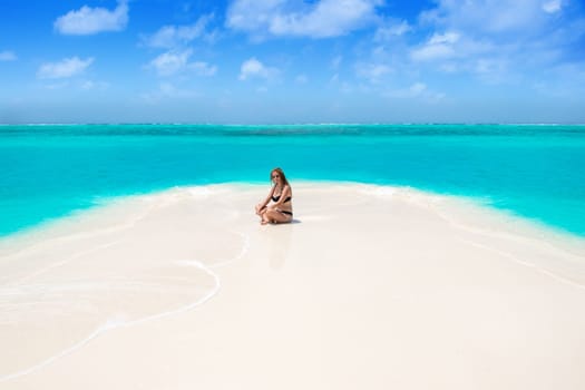 Blonde Girl in black bikini on dream beach at the turquoise ocean