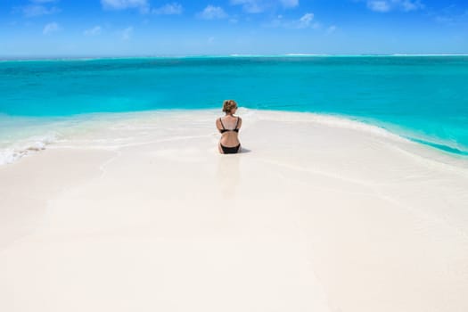 Blonde Girl in black bikini on dream beach at the turquoise ocean