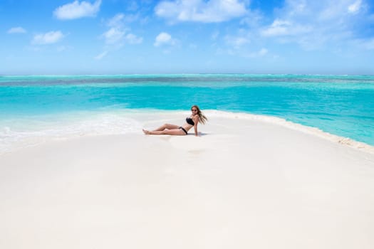 Blonde Girl in black bikini on dream beach at the turquoise ocean