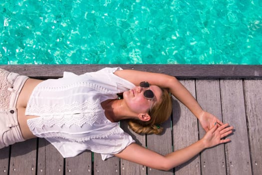 Young woman relaxes on a wooden walkway over turquoise ocean