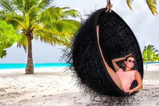 Beautiful woman relaxes on a swing on the dream beach