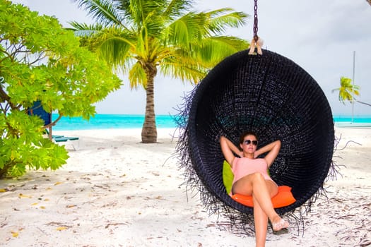 Beautiful woman relaxes on a swing on the dream beach