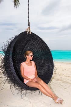 Beautiful woman relaxes on a swing on the dream beach