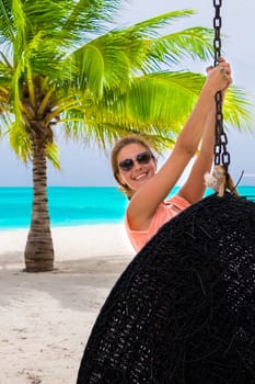 Beautiful woman relaxes on a swing on the dream beach
