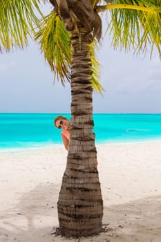 Gorgeous woman behind a palm tree at the dream beach