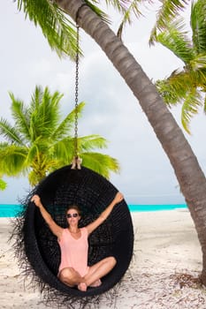 Beautiful woman relaxes on a swing on the dream beach