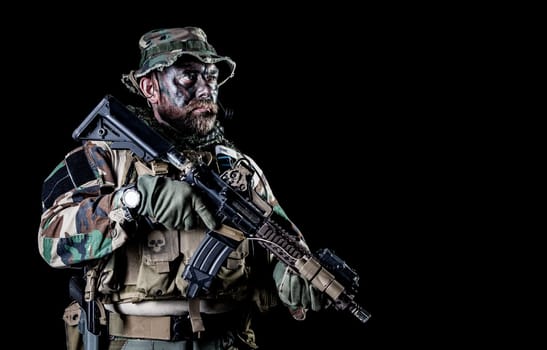 Bearded Special forces United States in Camouflage Uniforms studio shot half length black background. Holding weapons, wearing jungle hat, Shemagh scarf, he is ready to kill. Backlit