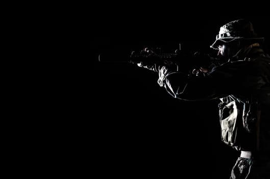 Bearded Special forces United States in Camouflage Uniforms studio shot half length black background, backlit. He is shooting killing enemy, pointing the rifle