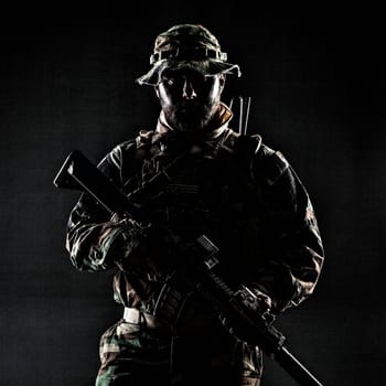 Bearded Special forces United States in Camouflage Uniforms studio shot half length. Holding weapons, wearing jungle hat, Shemagh scarf, he is ready to kill. Contour shot, backlit