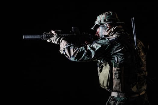 Bearded Special forces United States in Camouflage Uniforms studio shot half length black background, backlit. He is shooting killing enemy, pointing the rifle