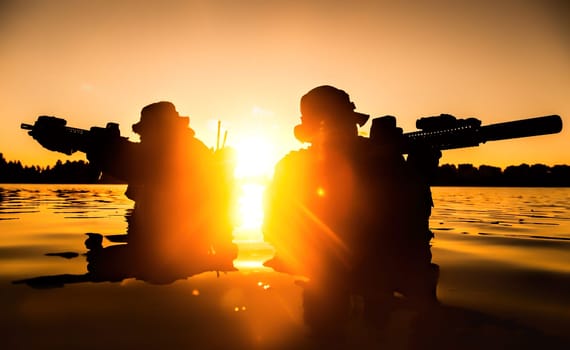 Silhouette of special forces with rifle in action during river raid in the jungle waist deep in the water. Proflie side view, half length