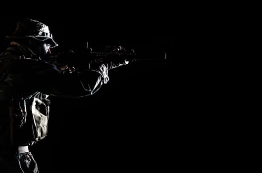 Bearded Special forces United States in Camouflage Uniforms studio shot half length black background, backlit. He is shooting killing enemy, pointing the rifle