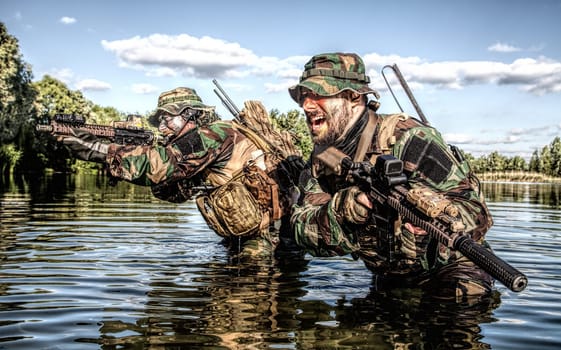 Pair of soldiers in action during river raid in the jungle waist deep in the water and mud and covering each other