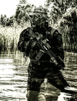 Bearded soldier of special forces in action during river raid in the jungle terrain. He is waist deep in the water and mud and ready to meet enemy, survive and fight in agressive hostile environment