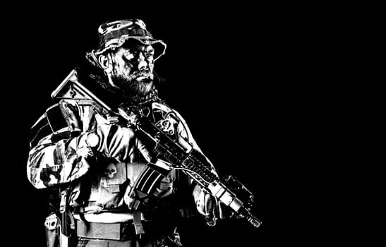 Bearded Special forces United States in Camouflage Uniforms studio shot half length black background. Holding weapons, wearing jungle hat, Shemagh scarf, he is ready to kill. Backlit