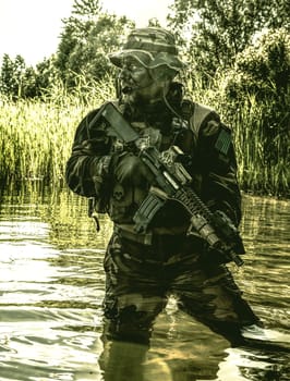 Bearded soldier of special forces in action during river raid in the jungle terrain. He is waist deep in the water and mud and ready to meet enemy, survive and fight in agressive hostile environment