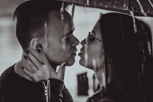 black white photo young couple standing under a dark umbrella.