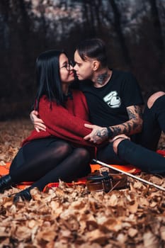 young man and young woman are sitting on a plaid in an autumn forest.