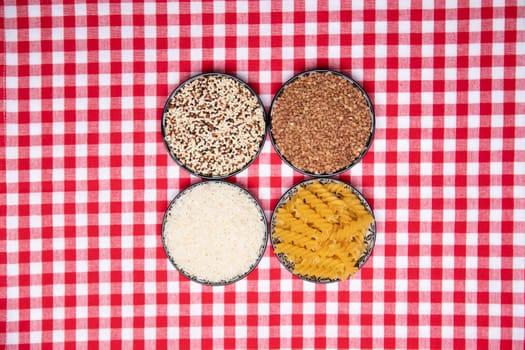 Vegetable food. A frame of four bowls with buckwheat, noodles, rice and quinoa on a red checkered tablecloth. Healthy eating. Top view with space for product montage.