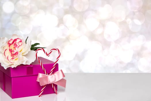 Happy Valentine or Mothers Day background. Red gift box with a beautiful white flower and red heart with bow ribbon on table over abstract bright bokeh backdrop. Space for your design.