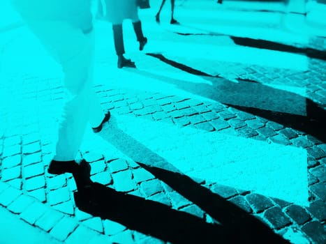 Blurry city zebra crossing with walking pedestrians legs making long shadows. Duotone effect with texture