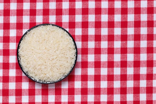 Vegetable food. Macro of a bowl with uncooked raw rice grains on a red checkered tablecloth. Healthy eating. Top view with space for product montage.