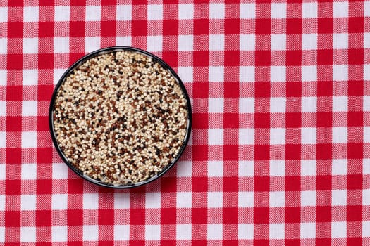 Vegetable food. Macro of a bowl with uncooked raw tricolor quinoa grains on a red checkered tablecloth. Healthy eating. Top view with space for product montage.