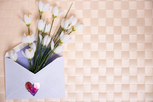 Happy Valentine or Mothers Day background. Beautiful bouquet of white flowers in an open envelope with a hearts symbol lying on a bright table. Space for your design on the right side.