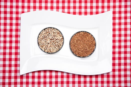 Vegetable food. A decorative white plate with two bowls with buckwheat and quinoa on a red checkered tablecloth. Healthy eating. Top view.