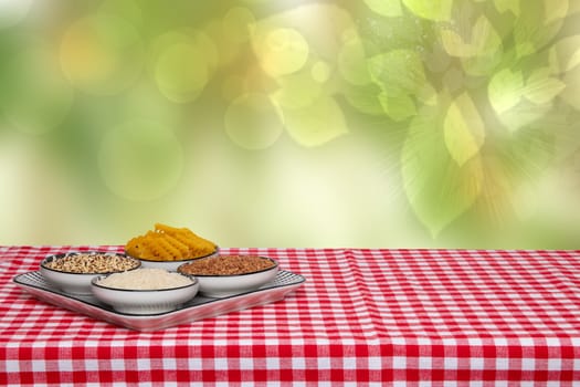 Table top on vegetable food background. Four bowls with buckwheat, noodles, rice and quinoa on a red checkered tablecloth over abstract bright green spring backdrop. Template for display product montage.