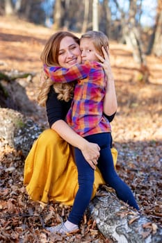 Happy mother and serious daughter hugging each other in the autumn nature background