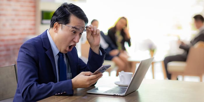 Portrait of Asian Businessman celebrate and glad for his success in cafe using smart phone and laptop with business team in background using for coporate background work, panoramic web banner composition